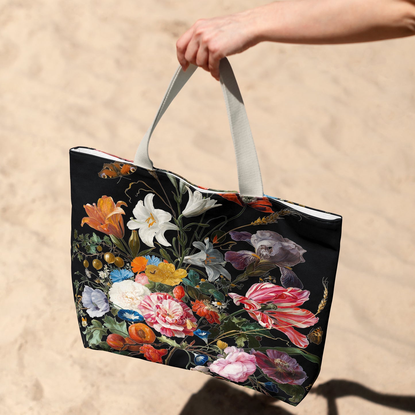 Tote bag with floral design held by a hand on a sandy background
