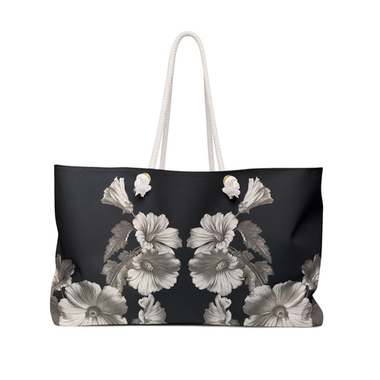 A black weekender tote with a floral pattern in shades of gray and white, featuring rope handles.