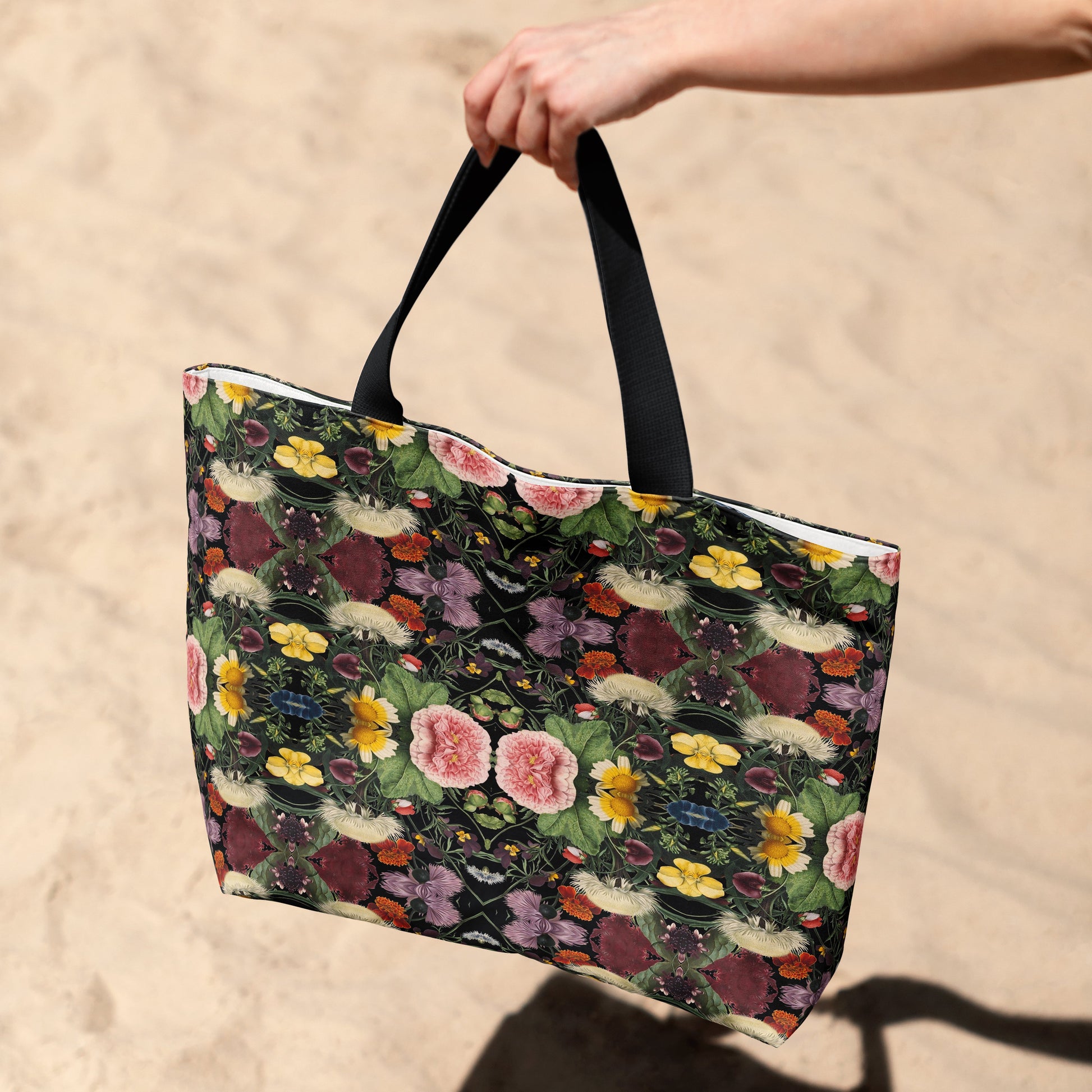 Floral-patterned tote bag held by a hand on a sandy background