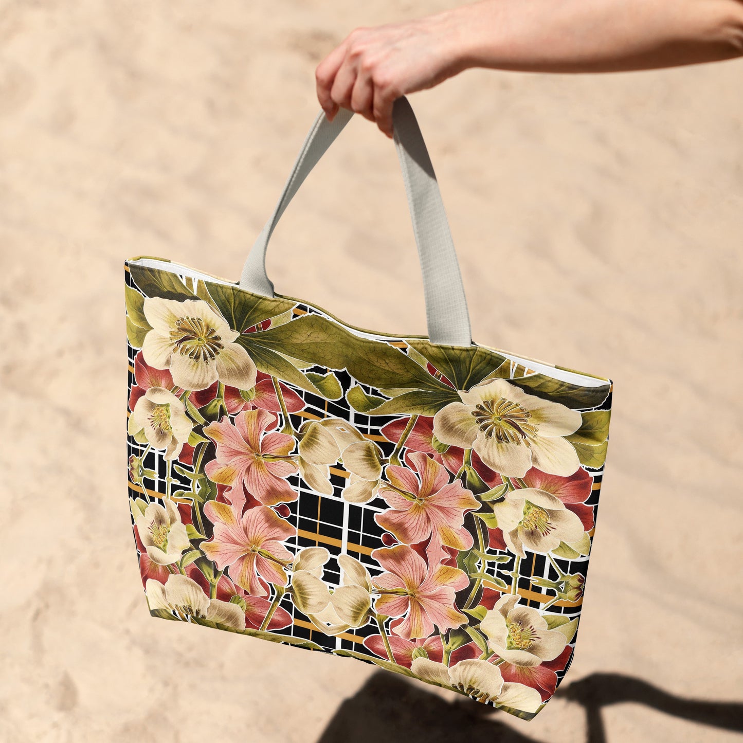 Tote bag with floral design held by a hand on a sandy background